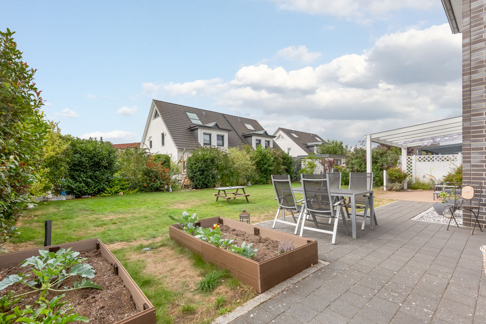 Garten mit Terrasse, Esstisch, Hochbeeten und Rasenfläche bei Wohnhäusern.