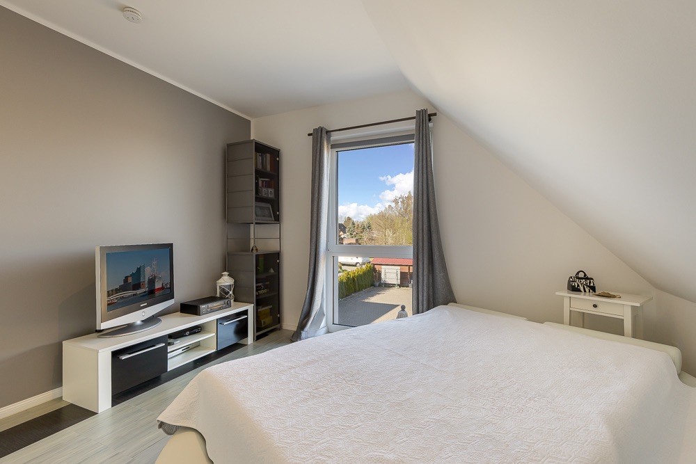 Schlafzimmer mit Doppelbett, Fenster, Fernseher und Nachttisch unter Dachschräge.