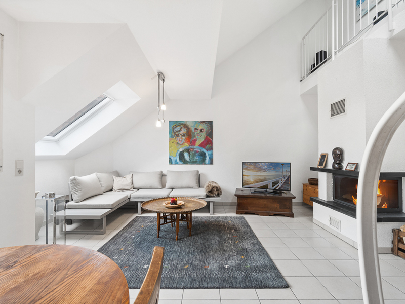 Helles Wohnzimmer mit Ecksofa, Kamin, Teppich, TV, rundem Tisch und Wandbild.