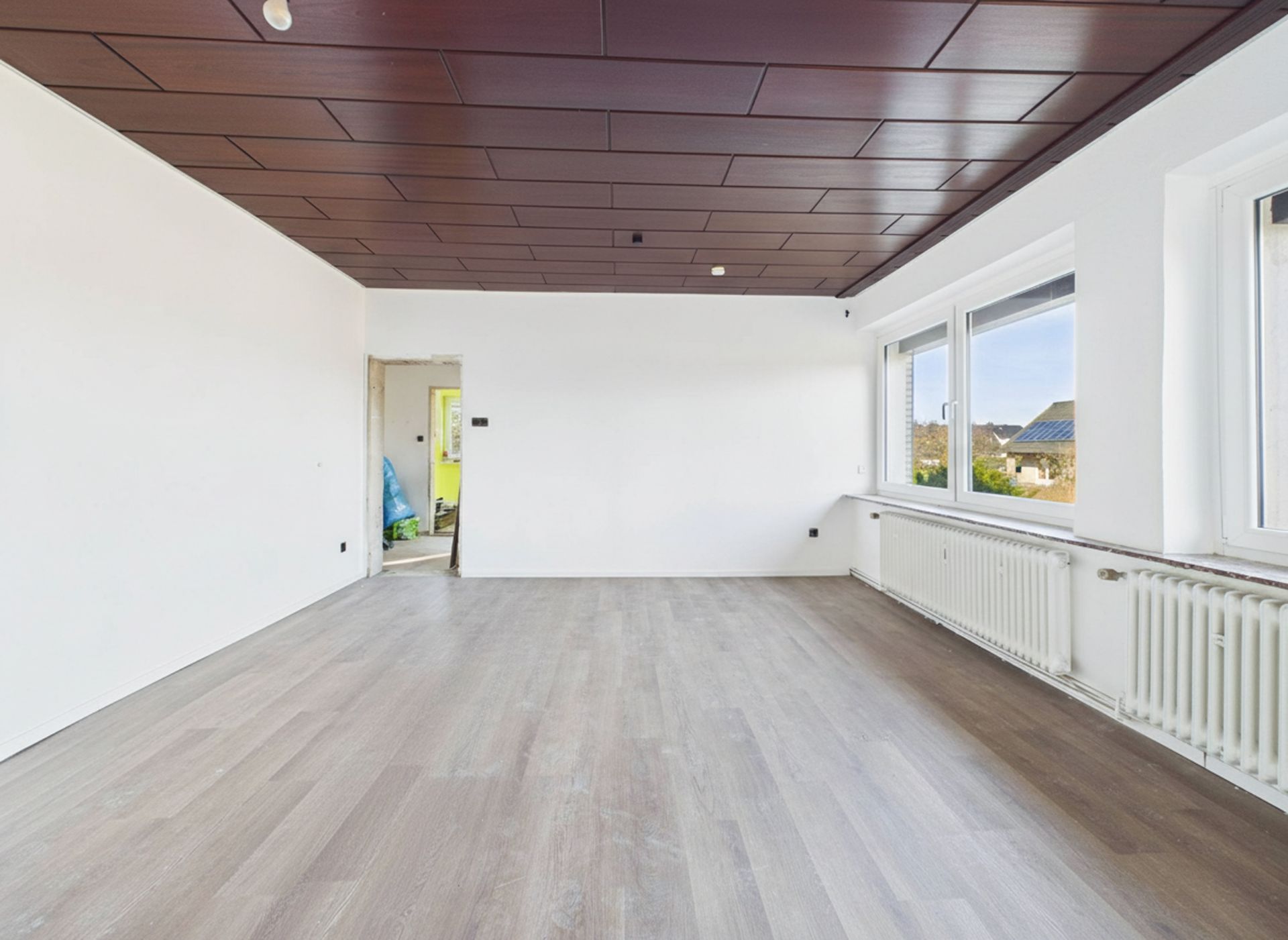 Leerer Raum mit Holzfußboden, weißen Wänden, großen Fenstern und dunkler Decke.
