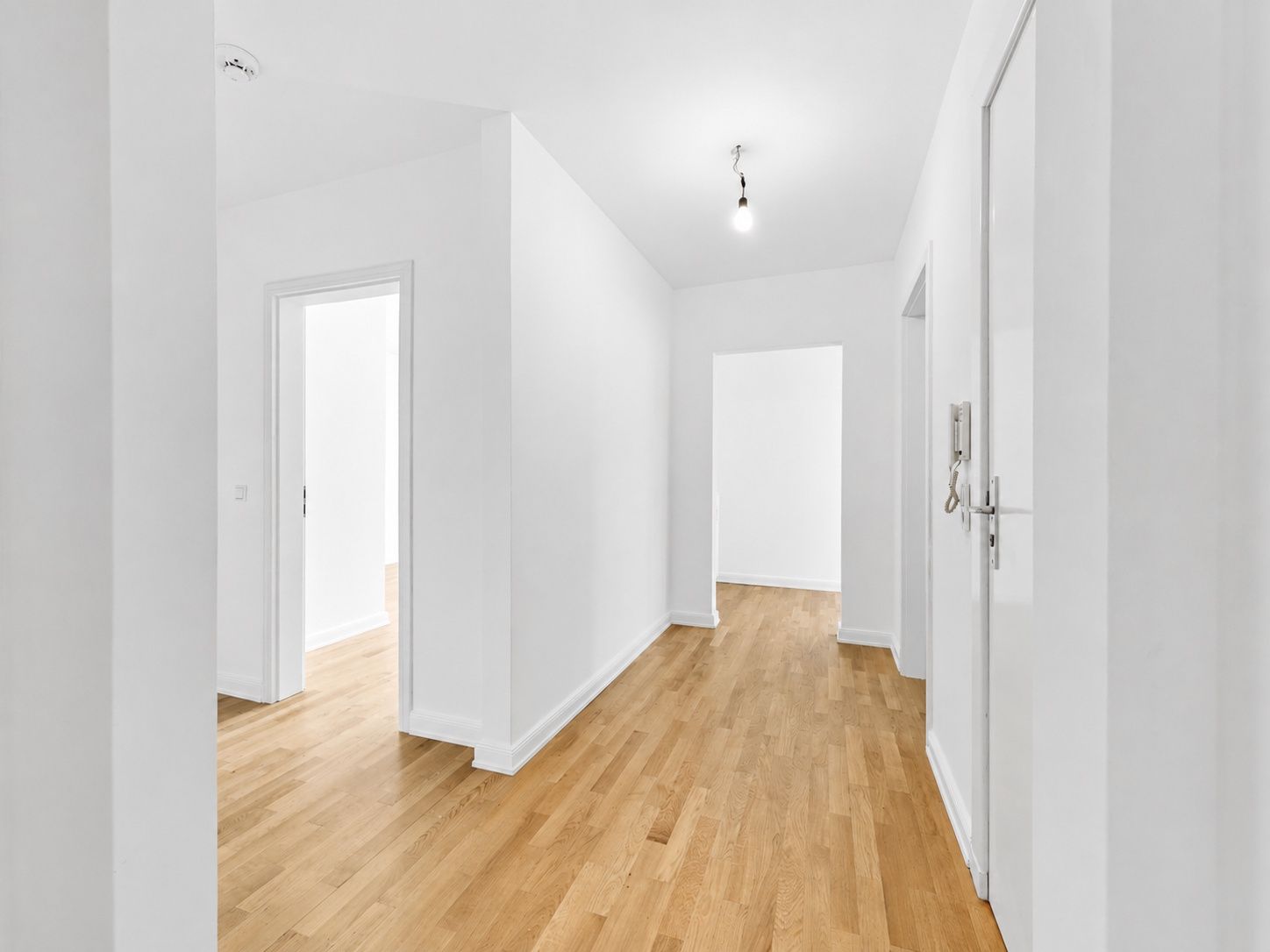 Heller Flur mit Holzboden, weißen Wänden und mehreren Türen in einer Wohnung.