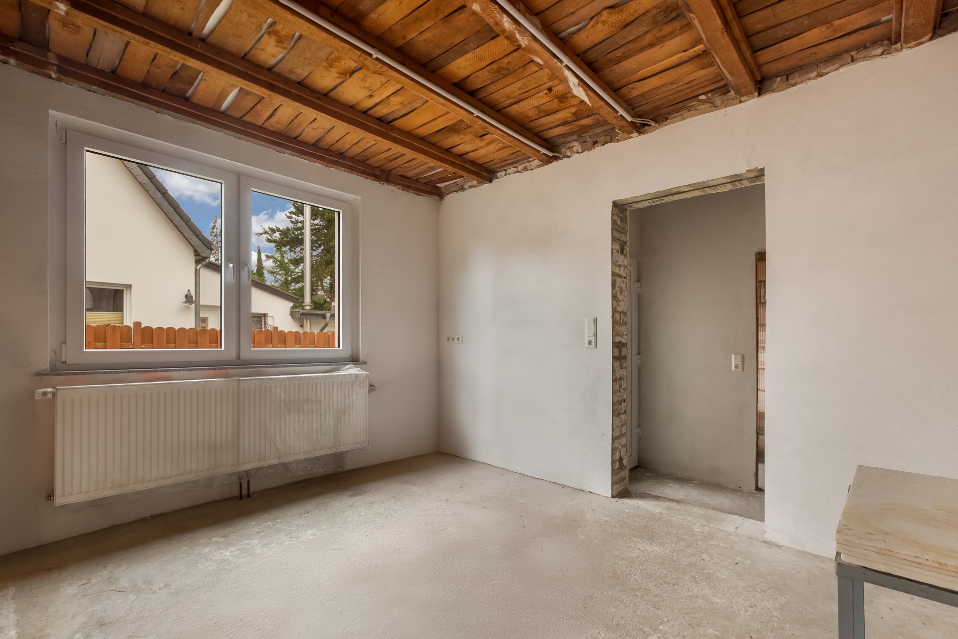 Leerer Raum mit offener Decke, Fenster, Heizung und Türöffnung.
