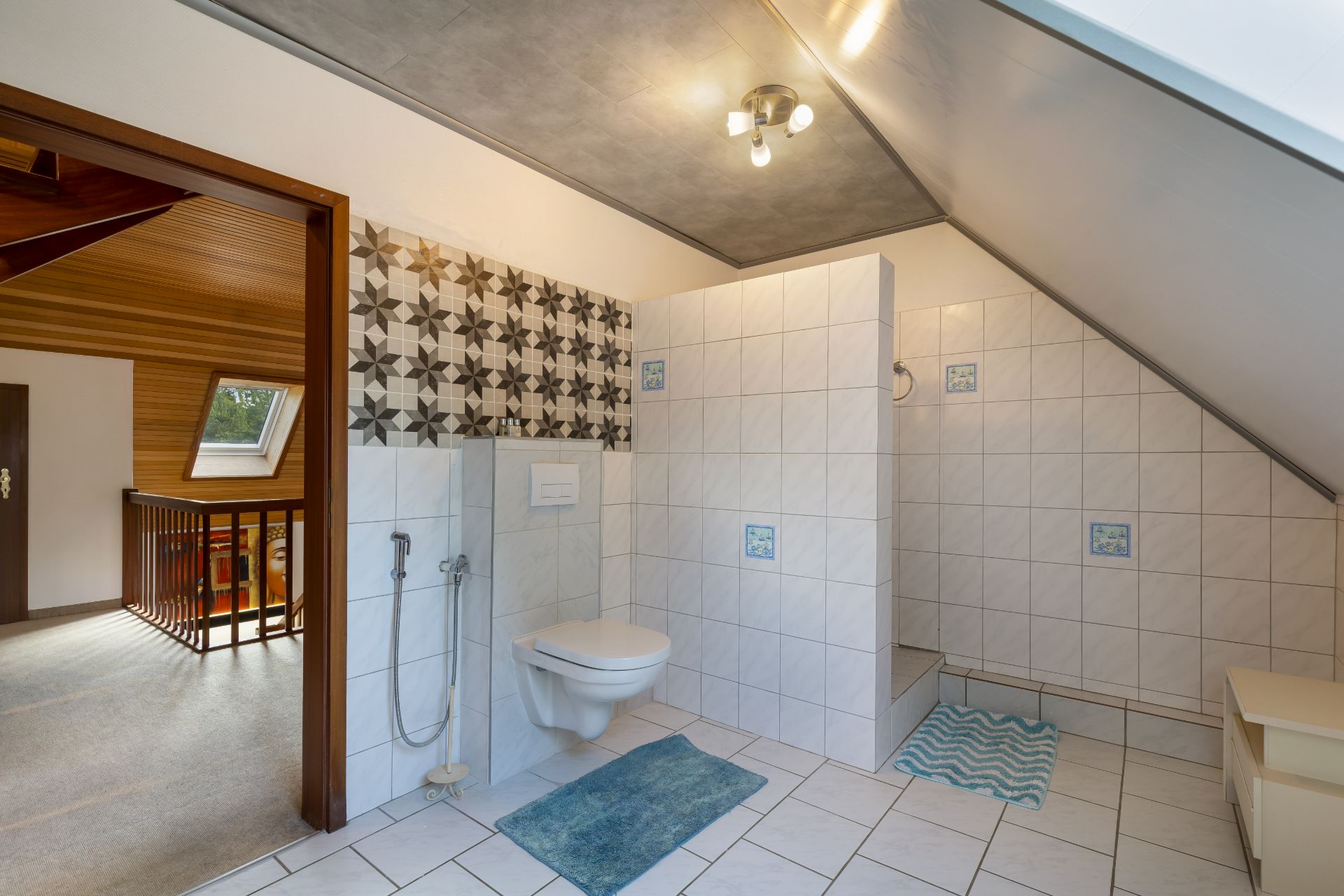 Modernes Badezimmer mit WC, gefliester Dusche und gemusterten Wandfliesen im Dachgeschoss.