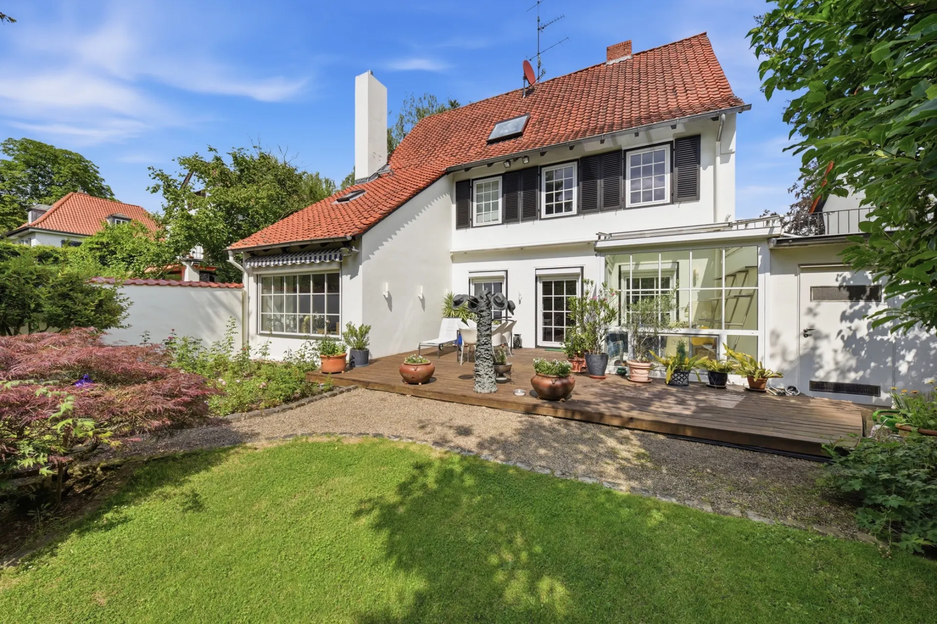Zweistöckiges Haus mit rotem Dach, Terrasse und Garten im Vordergrund.