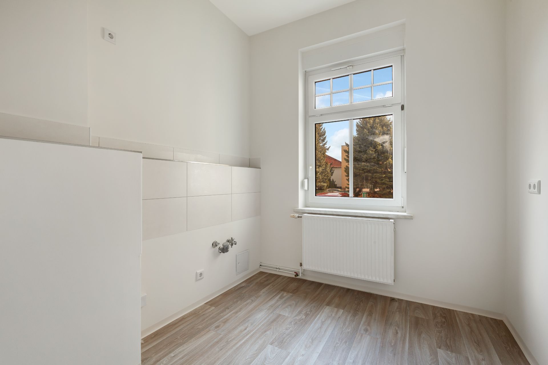 Leerer, heller Raum mit Holzboden, Fenster und Heizung unter dem Fenster.