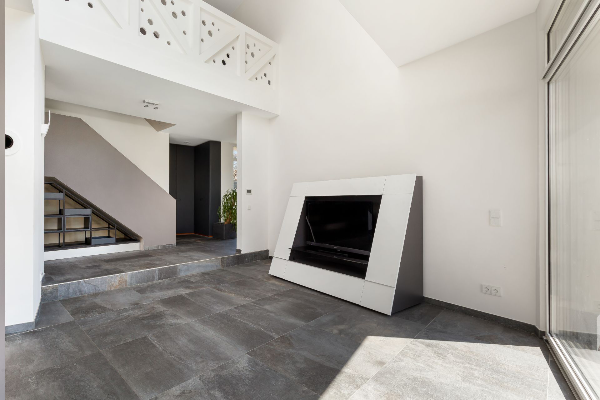 Heller Raum mit grauen Fliesen, modernem Kamin und Treppe im Hintergrund.