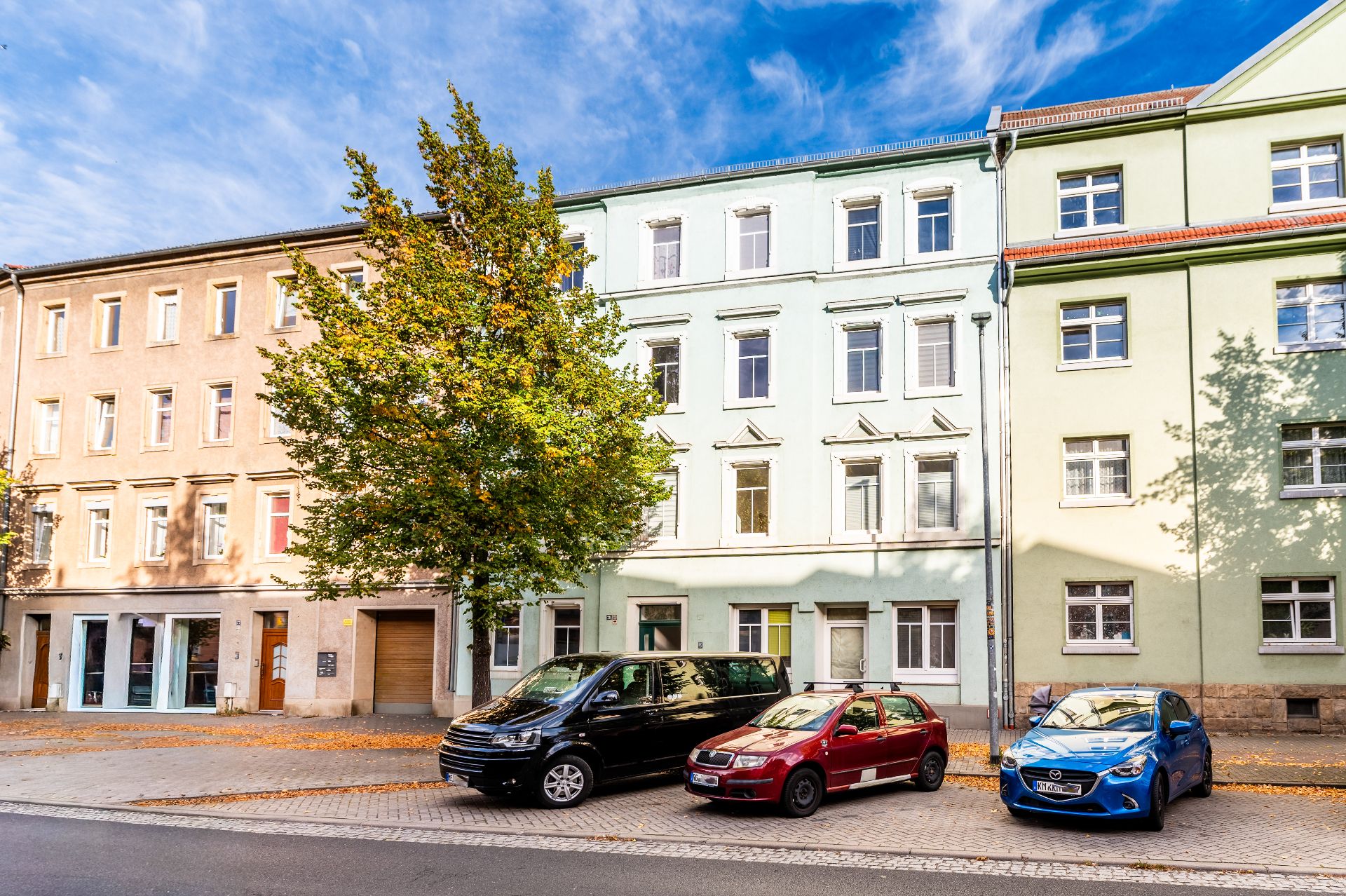 Mehrstöckiges Wohnhaus mit Bäumen und drei geparkten Autos davor.