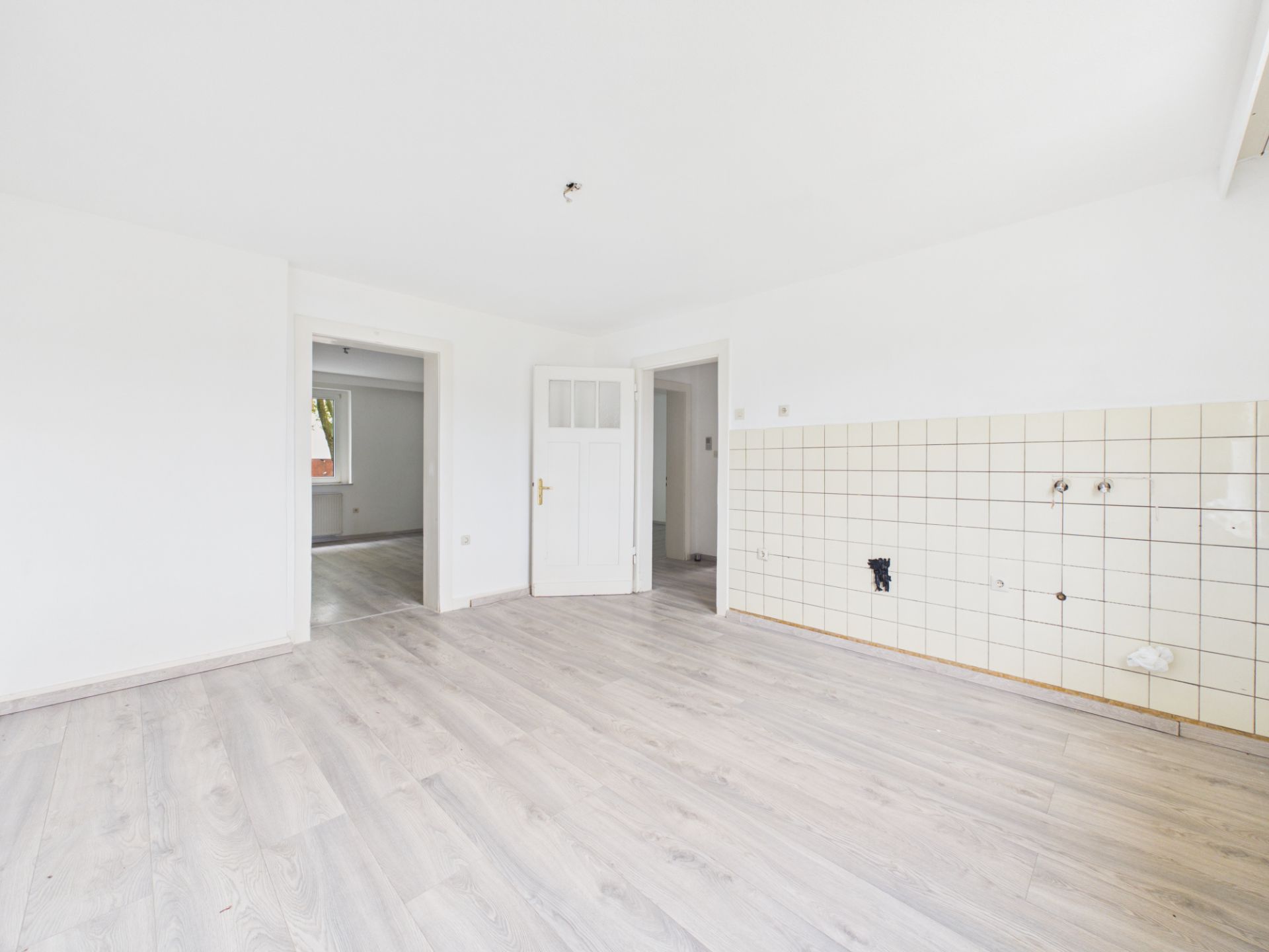 Leeres Zimmer mit hellen Wänden, Laminatboden und gefliester Wand auf der rechten Seite.
