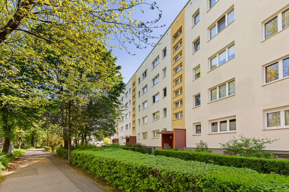 Mehrstöckiges Wohnhaus mit vielen Fenstern und grünem Gehweg davor.