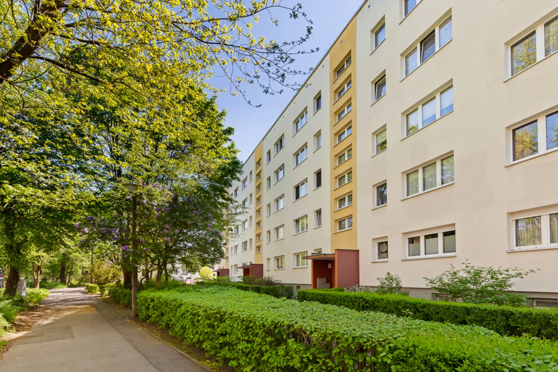 Mehrstöckiges Wohnhaus mit vielen Fenstern und grünem Gehweg davor.