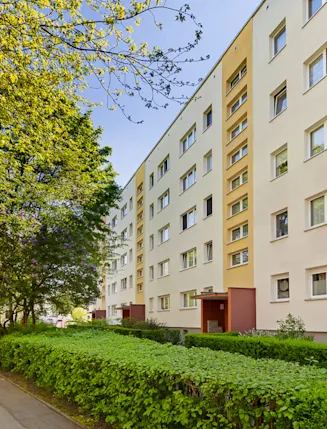 Mehrstöckiges Wohnhaus mit vielen Fenstern und grünem Gehweg davor.