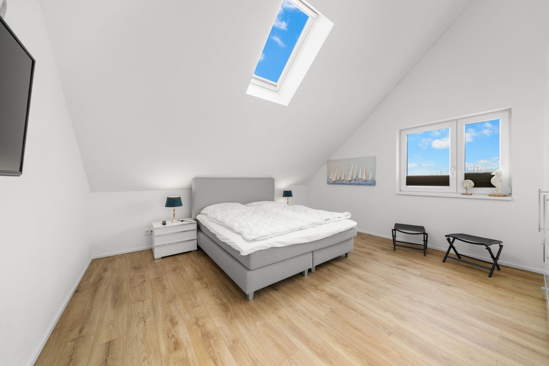 Helles Schlafzimmer mit Doppelbett, Dachfenster, Holzboden und zwei Nachttischen.