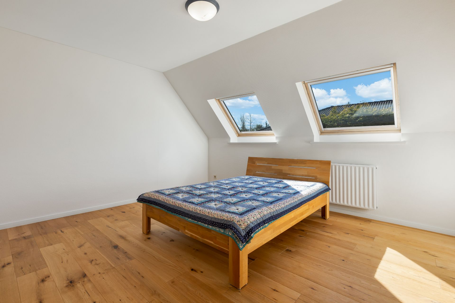 Schlafzimmer mit Holzfußboden, Doppelbett und zwei Fenstern im Dach.