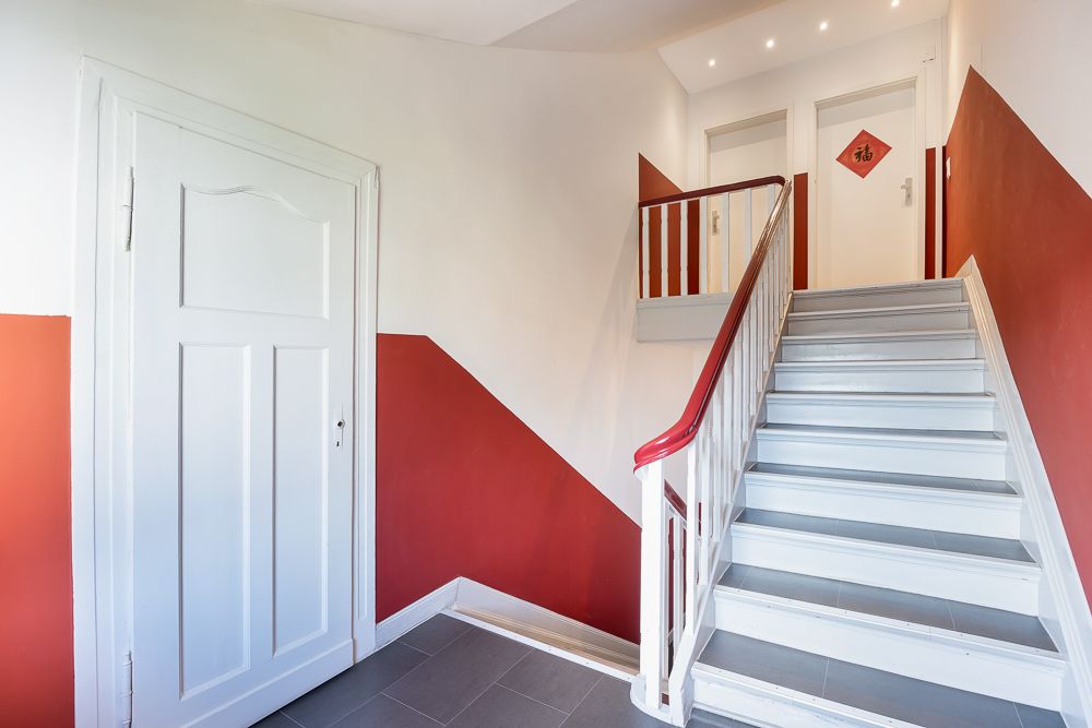Helles Treppenhaus mit rot-weißen Wänden und weißer Tür in einem Wohnhaus.