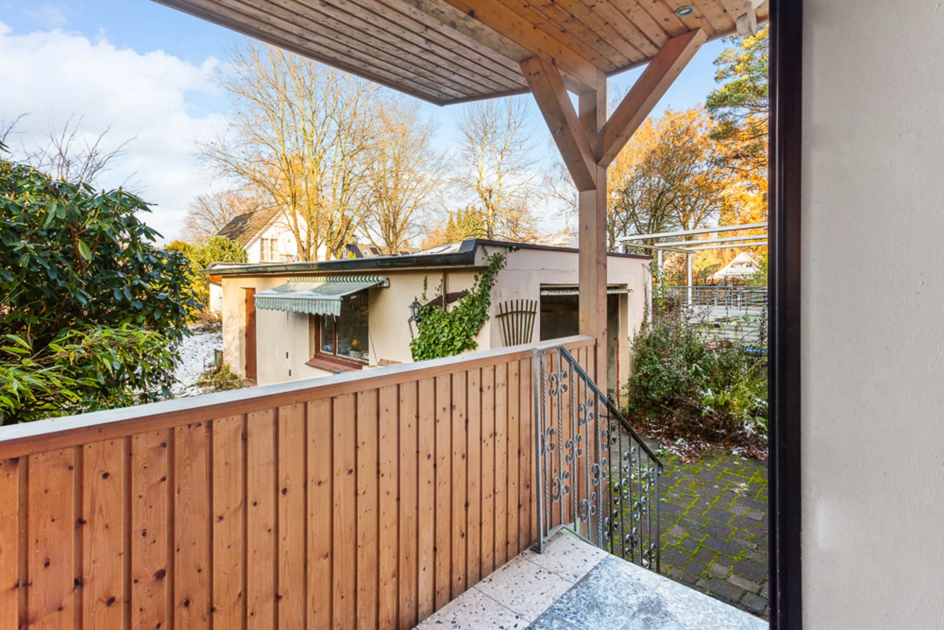 Überdachte Terrasse mit Holzgeländer, Blick auf Garten und Nebengebäude.
