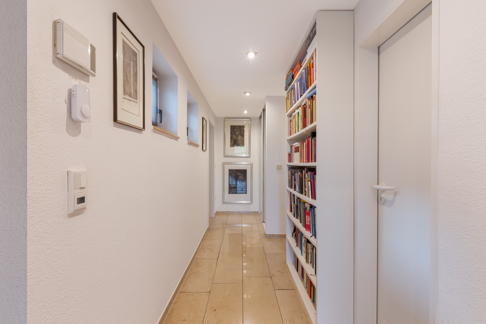 Heller Flur mit Bücherregal, weißen Wänden und mehreren Bildern an der Wand.