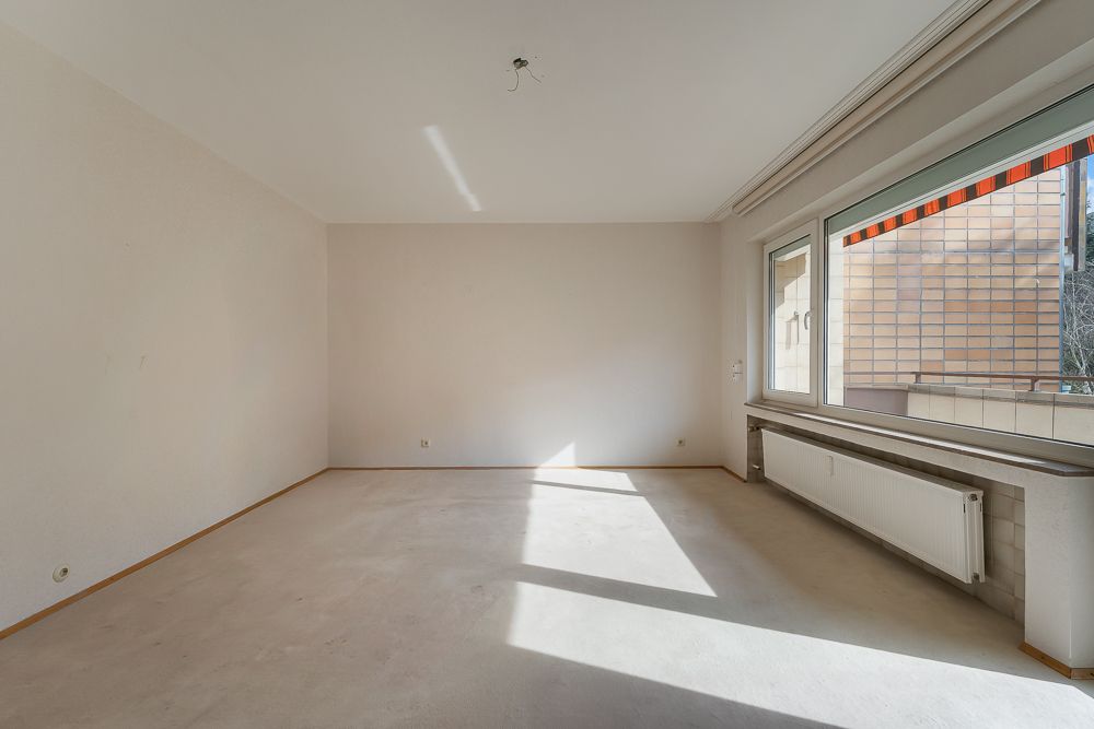 Leerer, heller Raum mit großem Fenster, weißem Heizkörper und Markise draußen.