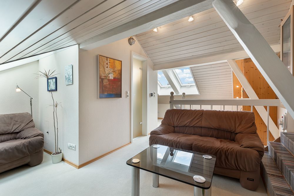 Wohnzimmer im Dachgeschoss mit braunen Sofas, Glastisch und Dachfenstern.