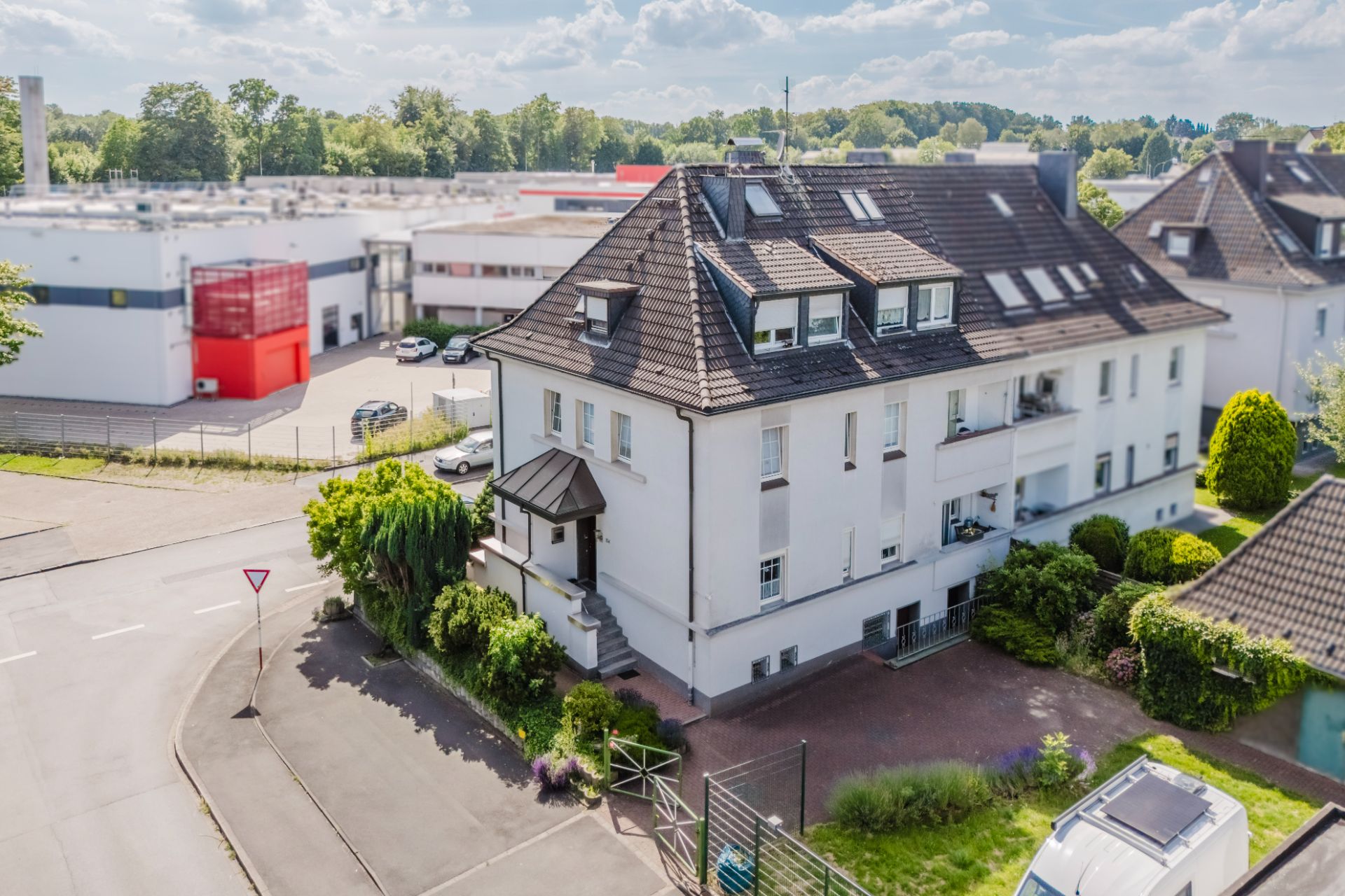 Großes, weißes Wohnhaus mit Garten, mehreren Fenstern und Balkonen an einer Straßenecke.