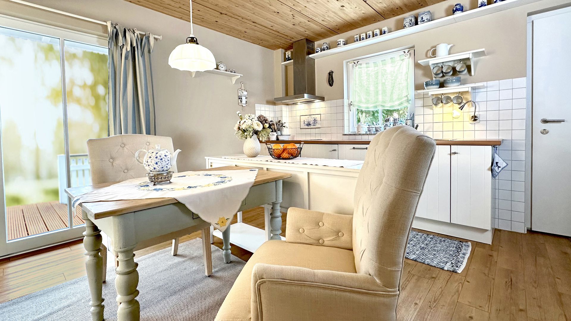 Helle Küche mit Holzboden, Esstisch, Polsterstühlen und Zugang zu einer Terrasse.