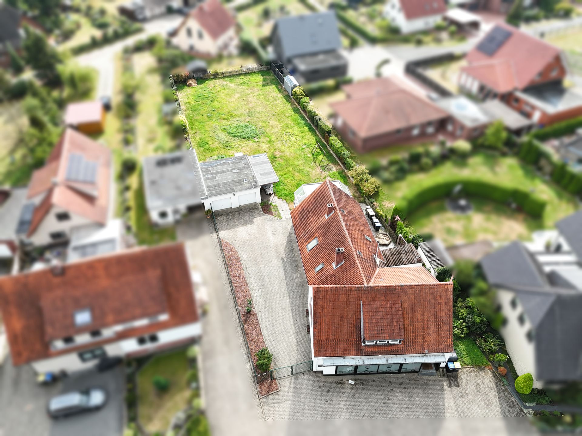 Luftaufnahme eines Einfamilienhauses mit rotem Dach und großem Garten.