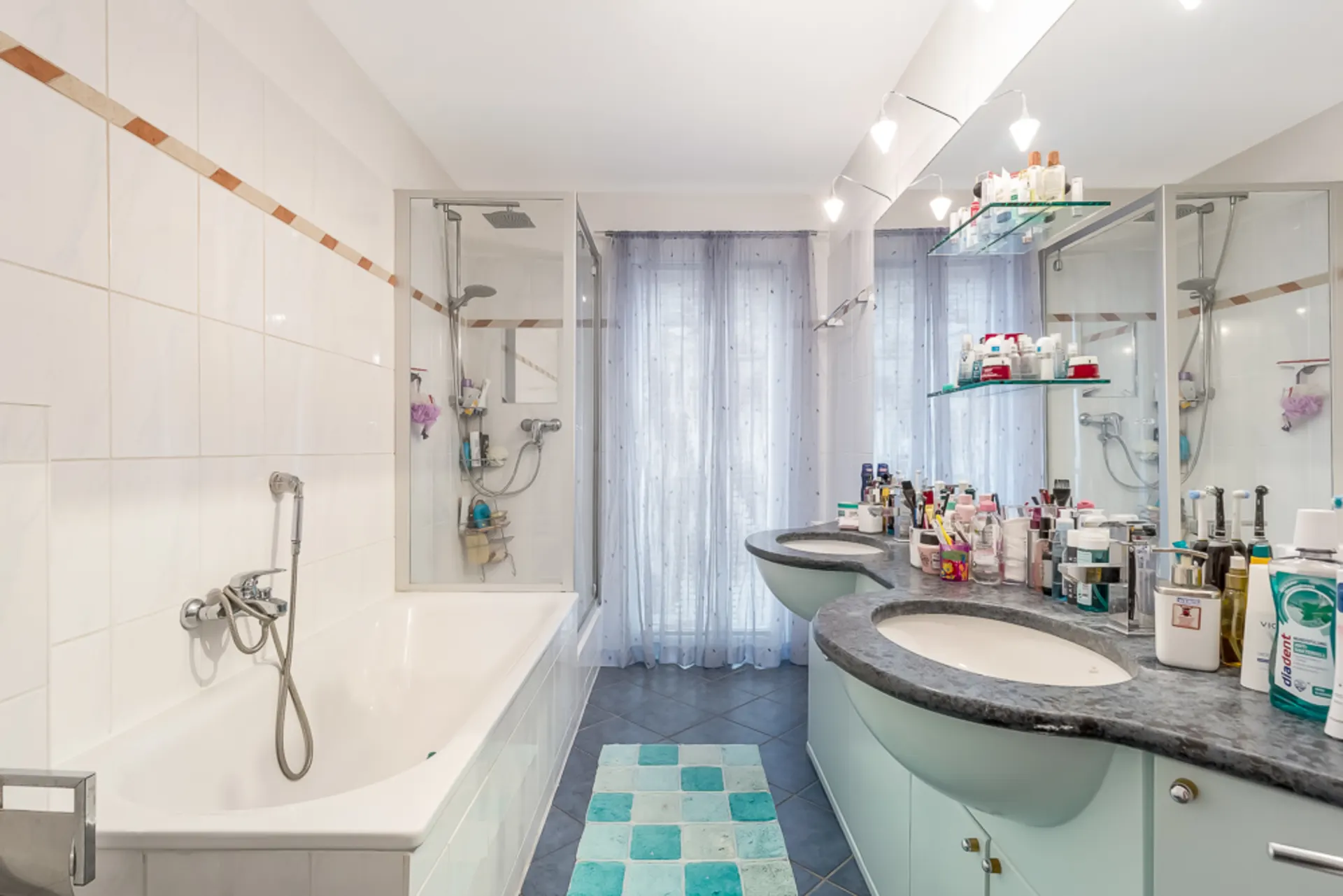 Modernes Badezimmer mit Badewanne, Doppelwaschbecken und vielen Pflegeprodukten auf der Ablage.