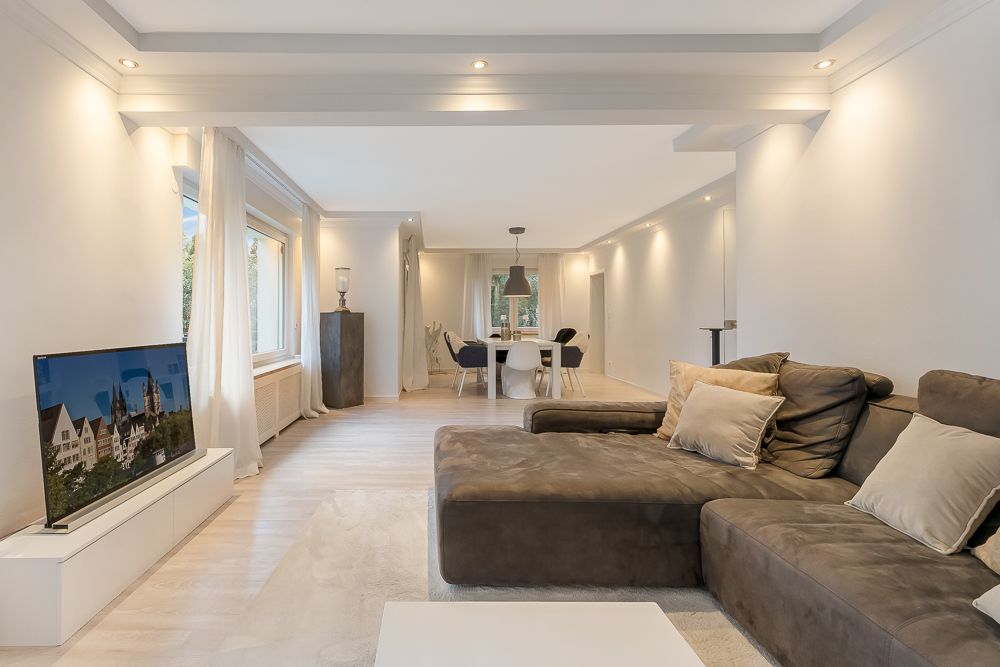 Modernes Wohnzimmer mit braunem Sofa, Fernseher und Essbereich im Hintergrund.
