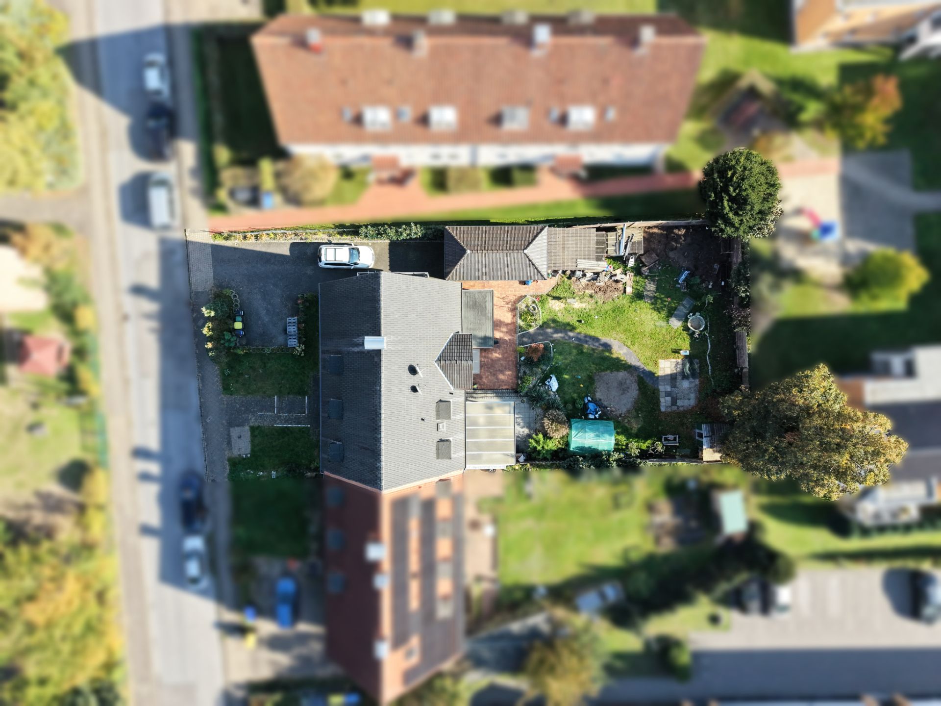 Vogelperspektive auf ein Wohnhaus mit Garten, Auffahrt und mehreren Bäumen.