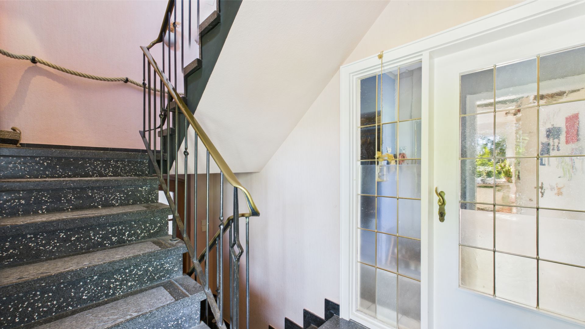 Treppenhaus mit schwarzer Steintreppe und Tür mit Glaseinsatz.