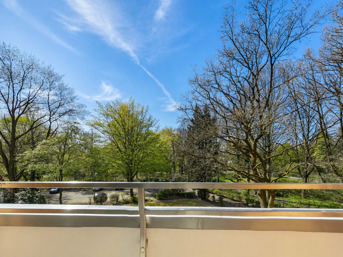 Blick von einem Balkon auf grüne Bäume und einen klaren, blauen Himmel.