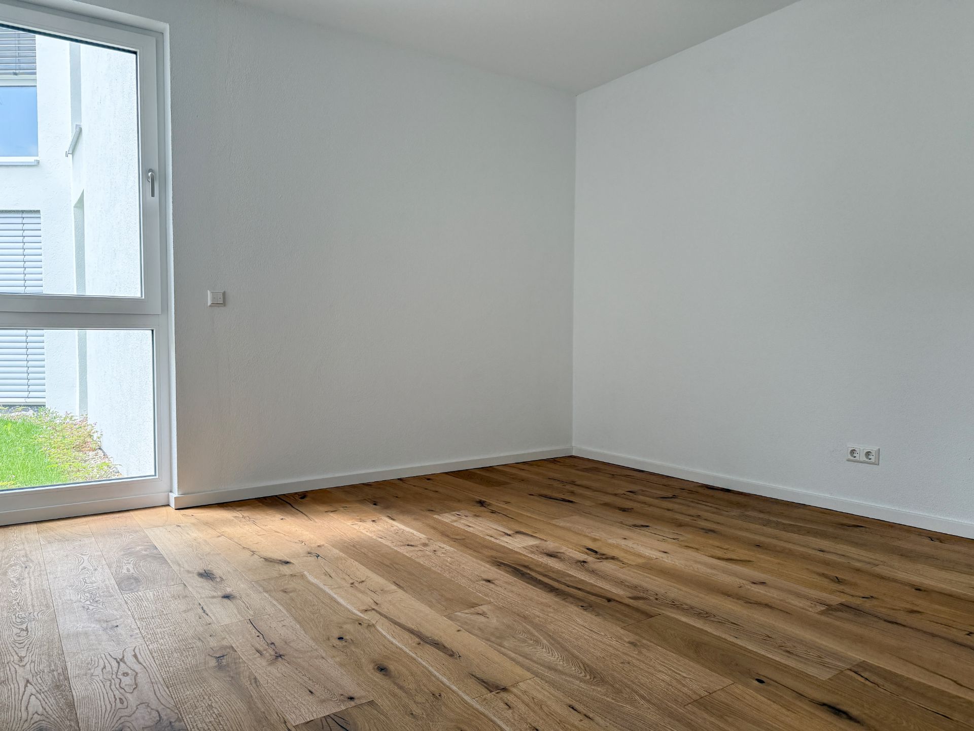 Leerer Raum mit Holzfußboden und großem Fenster, weiße Wände.