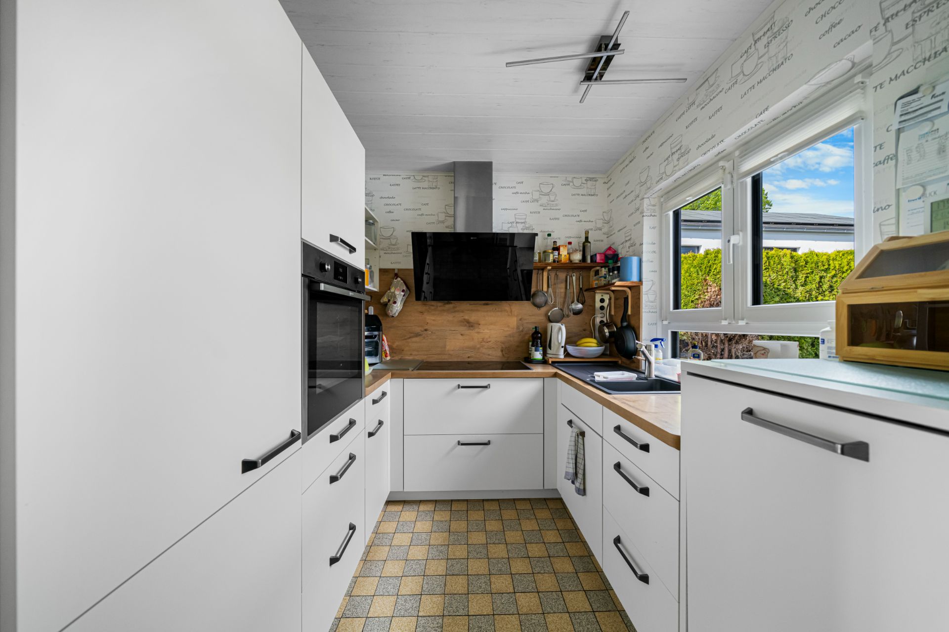 Moderne Küche mit weißen Schränken, Holzarbeitsplatte und großem Fenster.