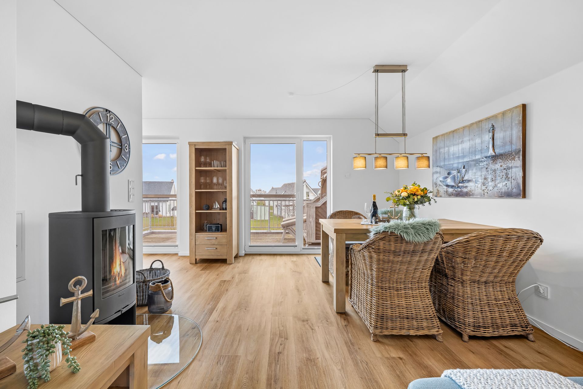 Helles Wohnzimmer mit Kamin, Esstisch, Korbstühlen und Zugang zu einem Balkon.