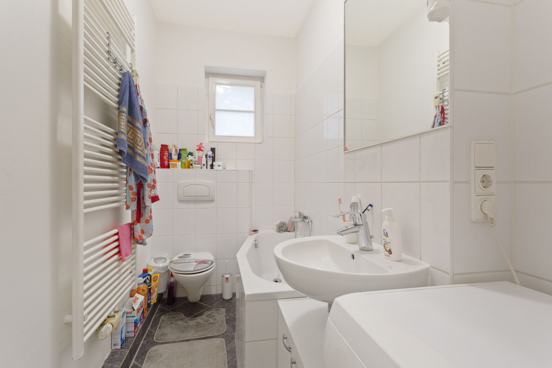 Badezimmer mit Waschbecken, Badewanne, Toilette, Handtuchheizung und kleinem Fenster.