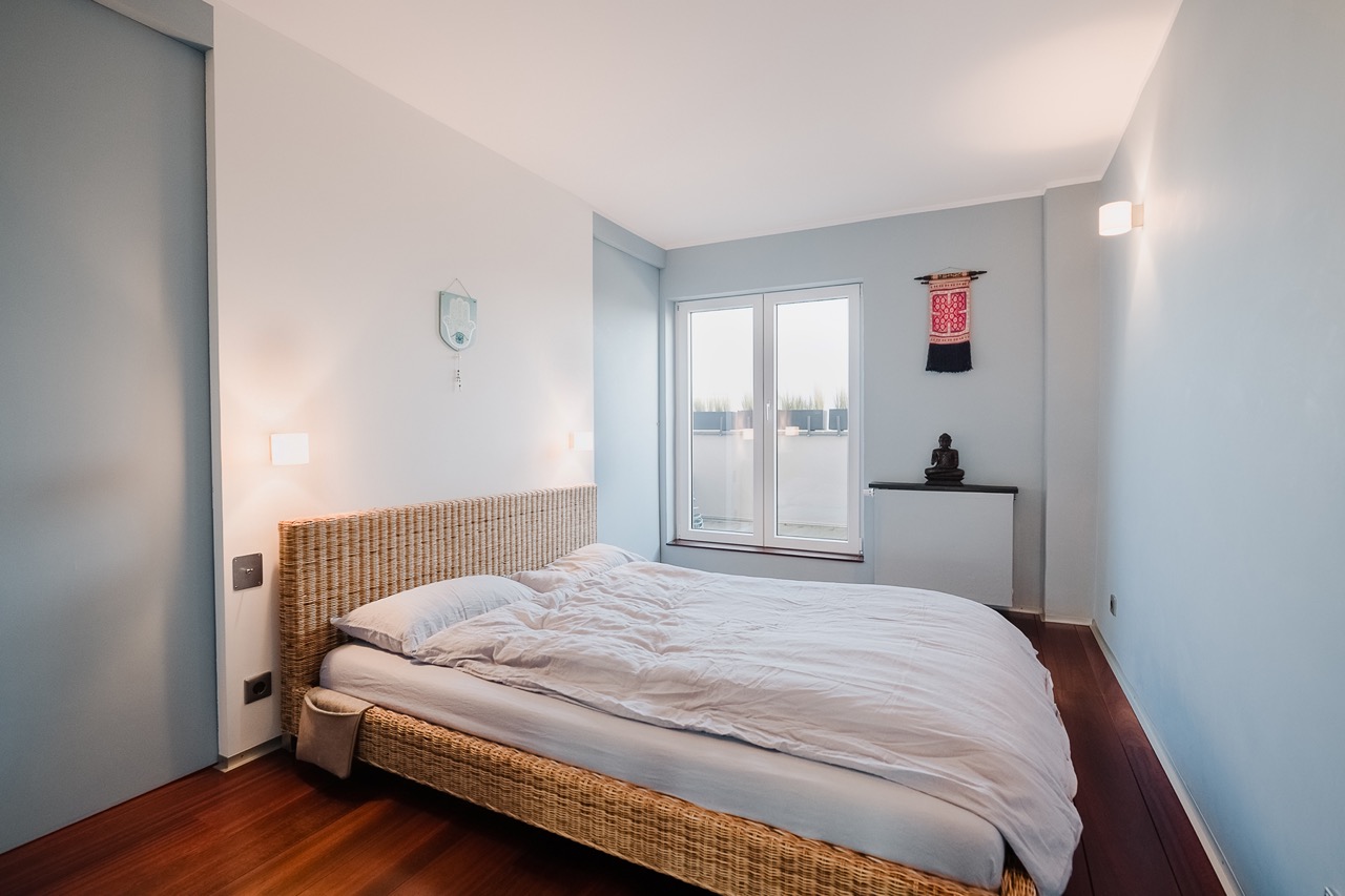 Helles Schlafzimmer mit großem Bett, Holzboden und bodentiefem Fenster.