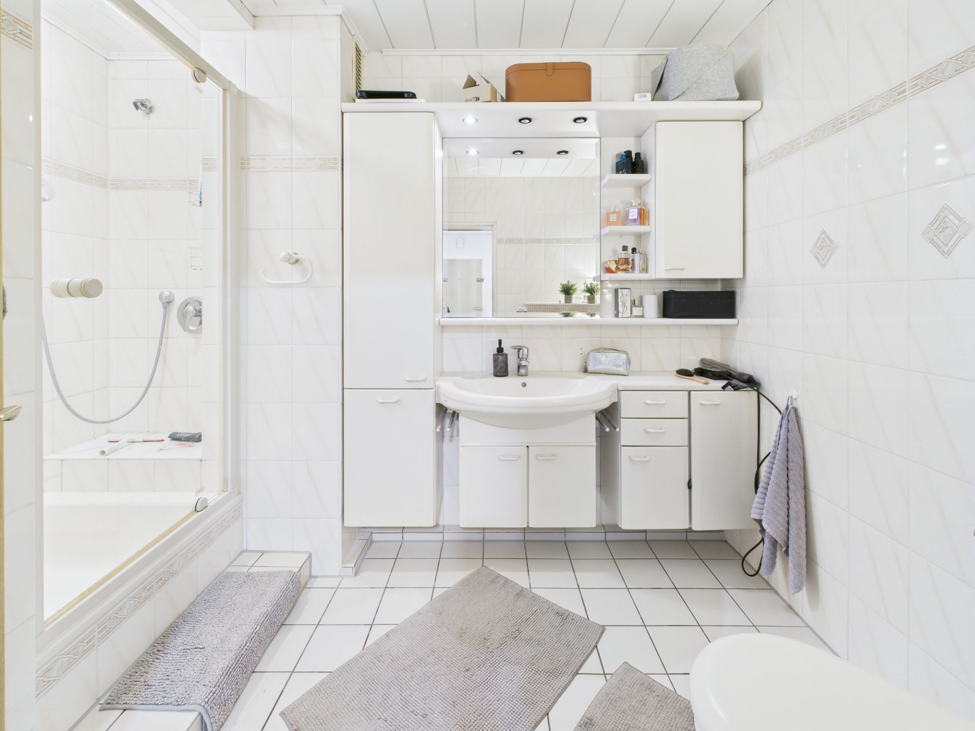 Helles Badezimmer mit Dusche, Waschbecken, Spiegelschrank und weißen Fliesen.