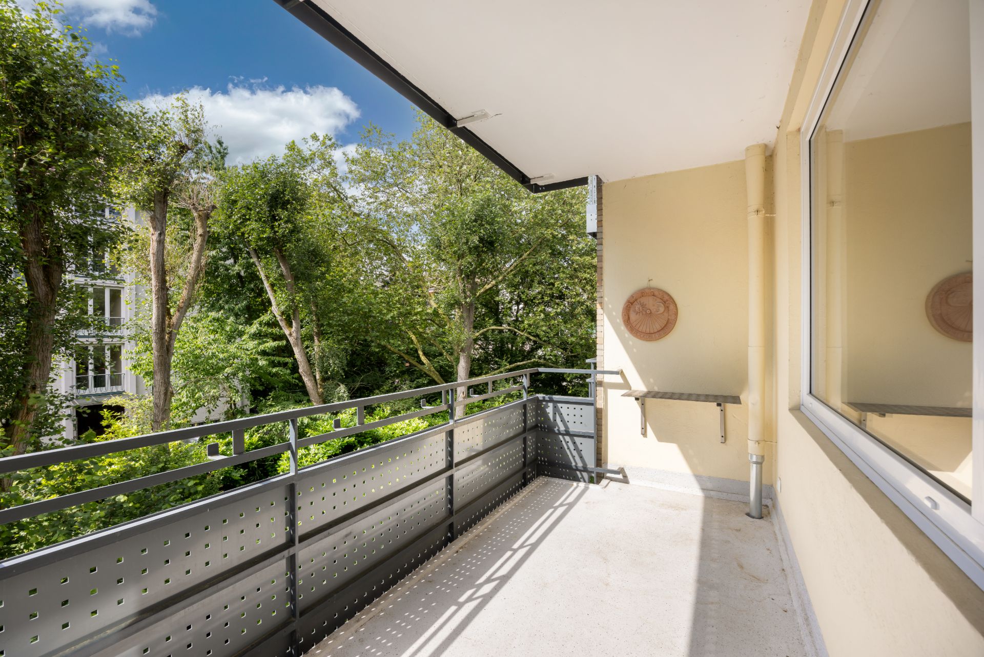 Geräumiger Balkon mit Metallgeländer und Blick auf grüne Bäume, sonnige Atmosphäre.
