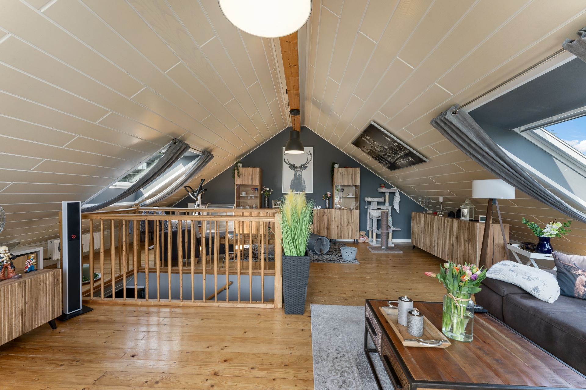 Heller Dachgeschossraum mit Holzfußboden, Sofa, Pflanzen und großen Dachfenstern.