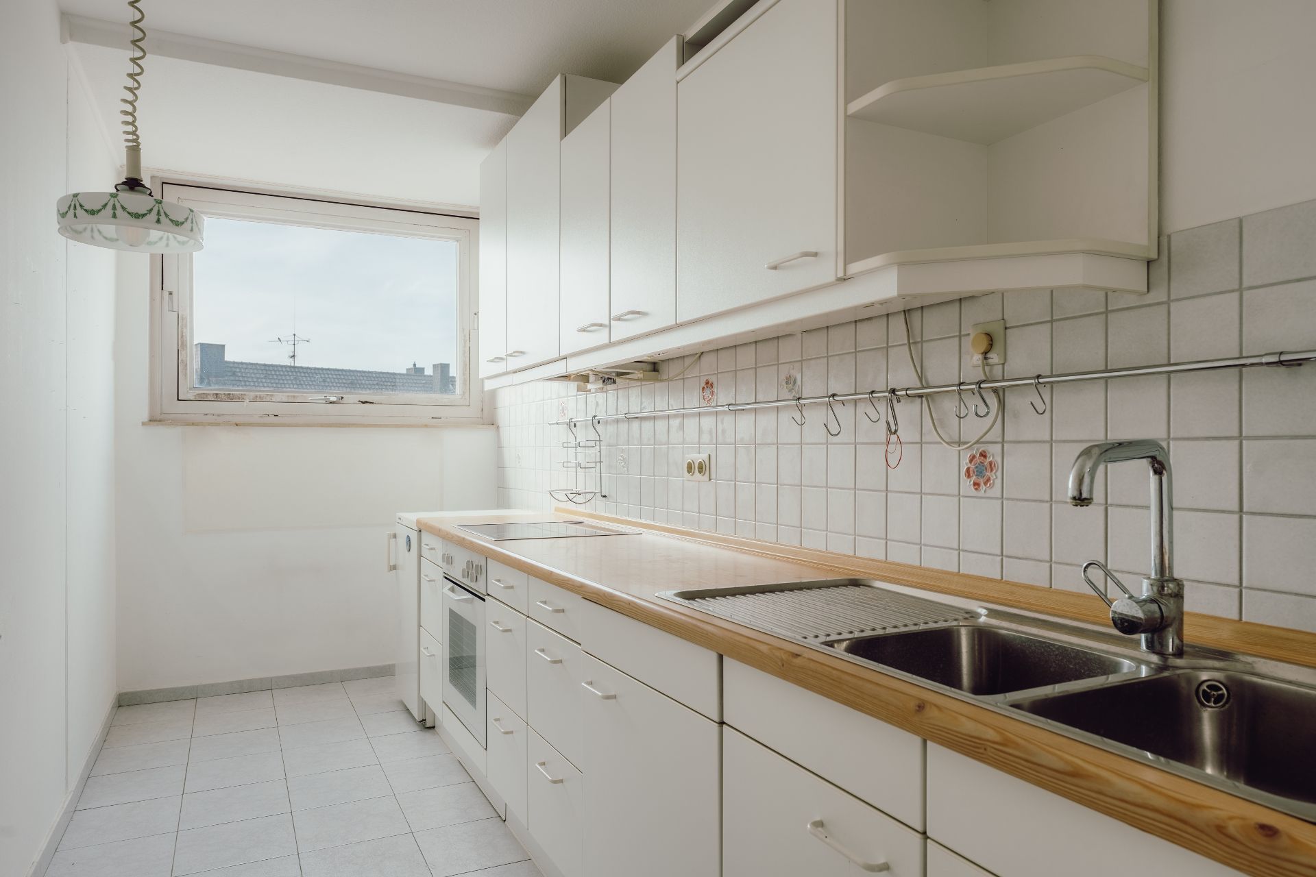 Helle Küche mit weißen Schränken, Holzarbeitsplatte, Herd, Spüle und großem Fenster.