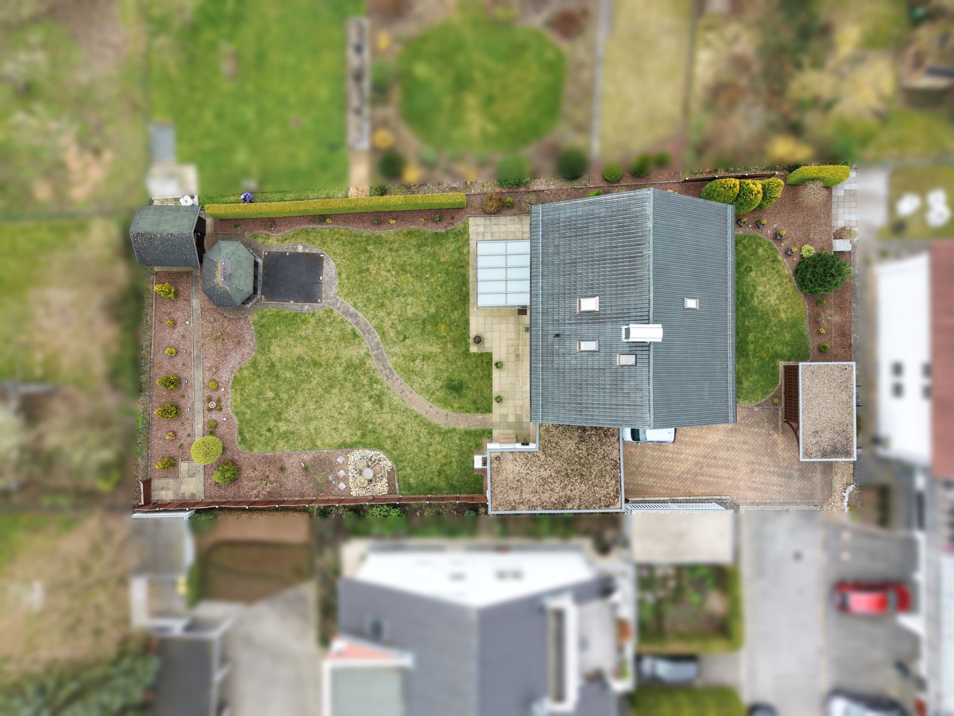 Luftaufnahme eines Hauses mit Garten, Terrasse, Wegen und Nebengebäuden.
