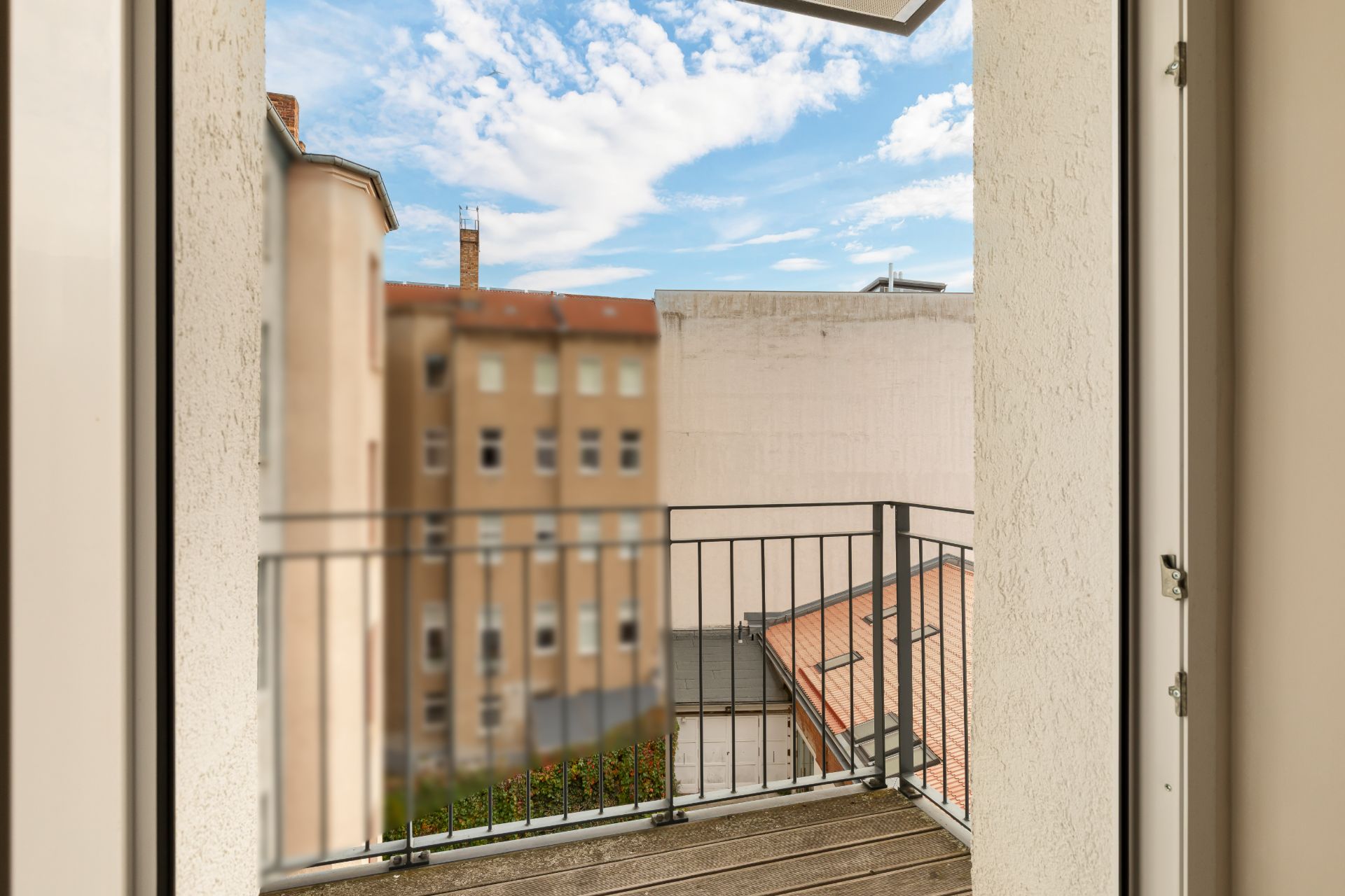 Blick von einem Balkon mit Metallgeländer auf Nachbargebäude und Himmel.