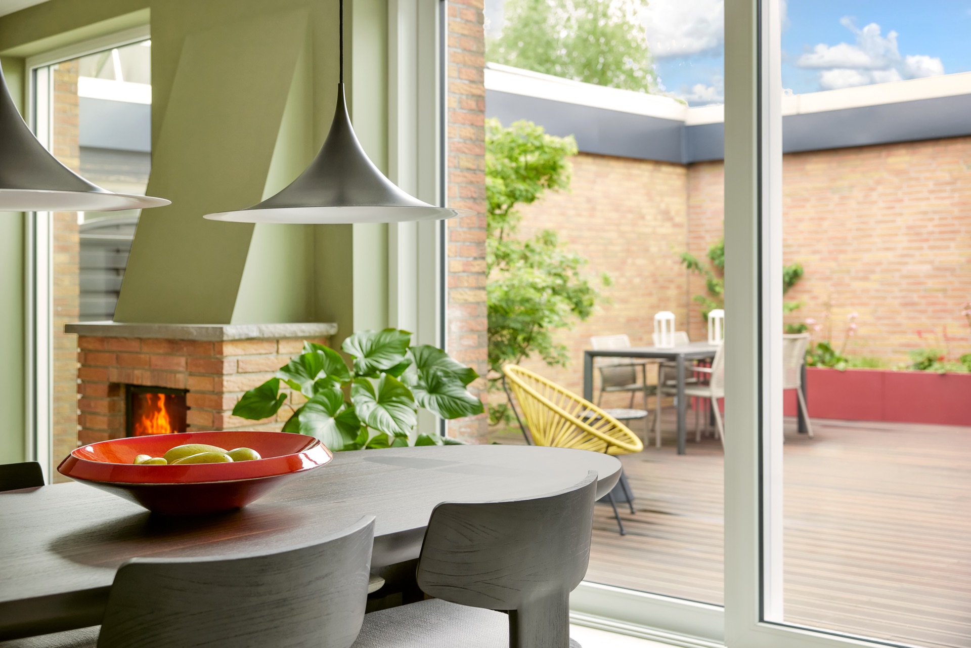 Essbereich mit Kamin, Tisch, Stühlen und Blick auf Terrasse mit Gartenmöbeln.
