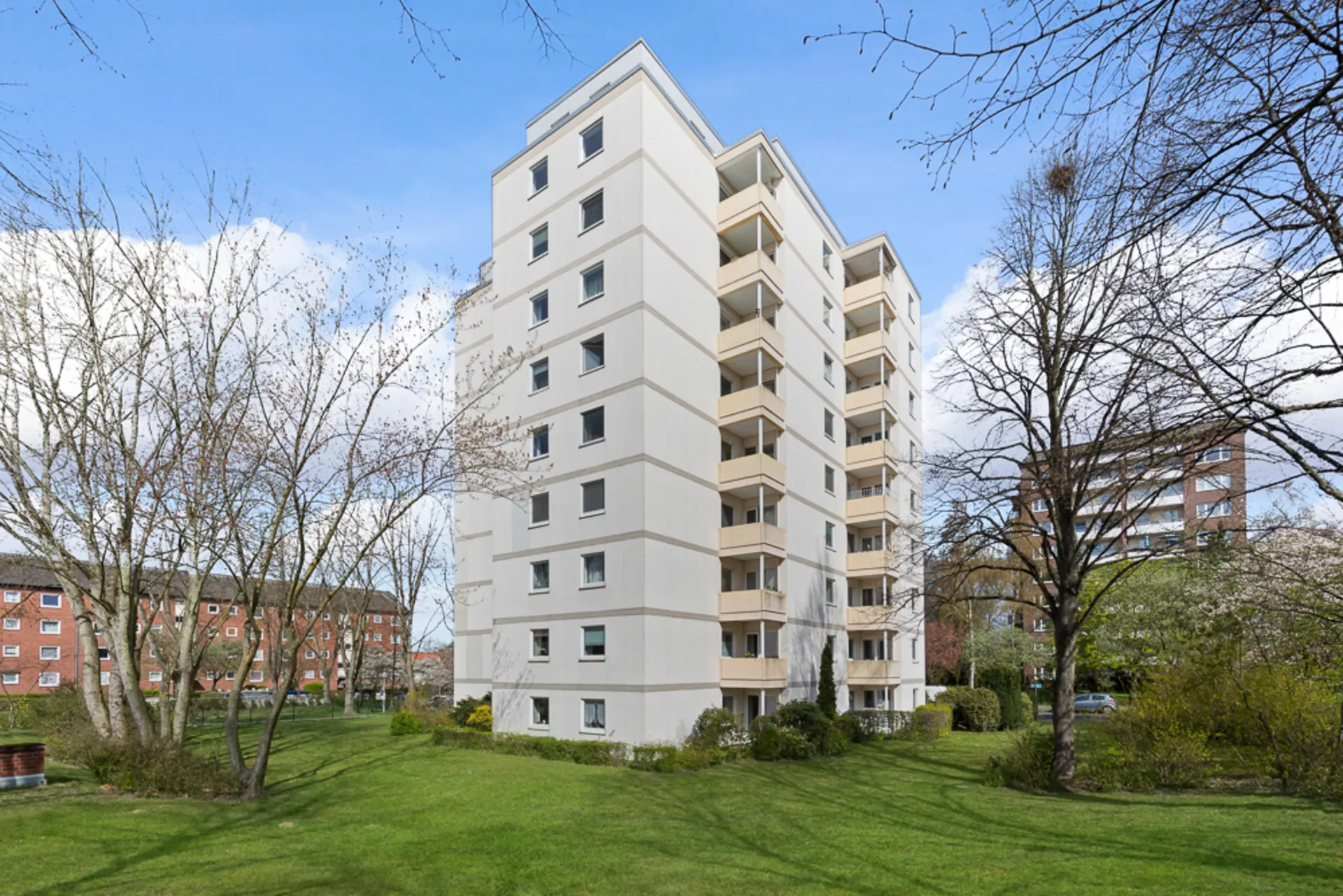 Mehrstöckiges Wohnhaus mit Balkonen und grüner Wiese im Vordergrund.