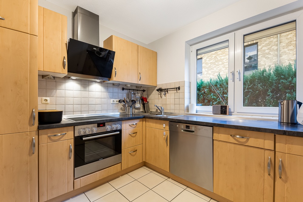 Moderne Einbauküche mit Holzmöbeln, Herd, Backofen, Spülmaschine und großem Fenster.