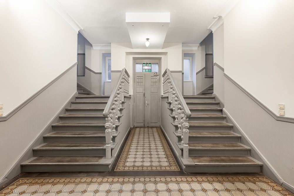 Eingangsbereich mit zwei grauen Treppen und Fliesenboden in einem Wohnhaus.