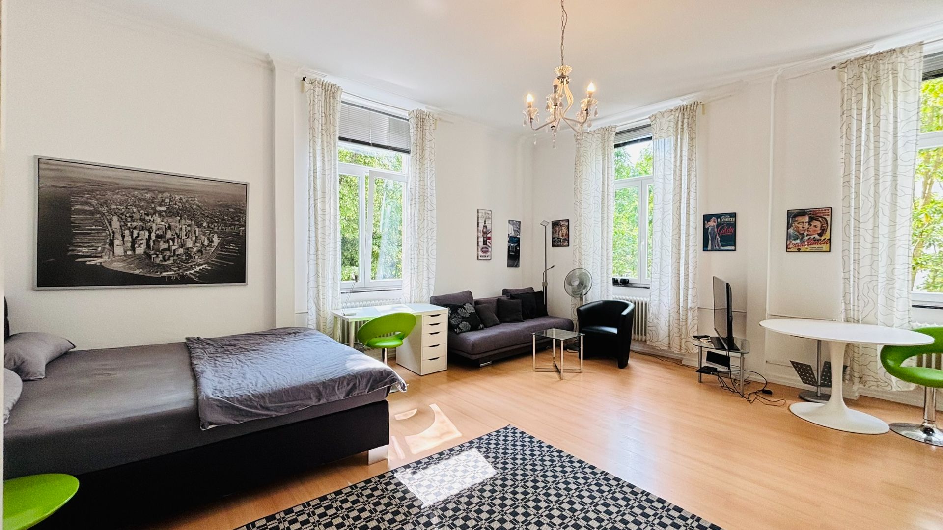 Helles Schlafzimmer mit Bett, Sofa, Teppich, Tisch und großen Fenstern mit weißen Vorhängen.