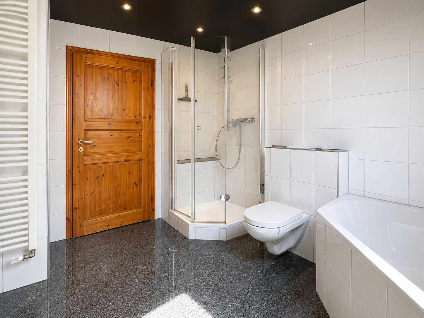 Modernes Badezimmer mit Dusche, Badewanne, WC und Holztür, weiße Fliesen an Wänden.