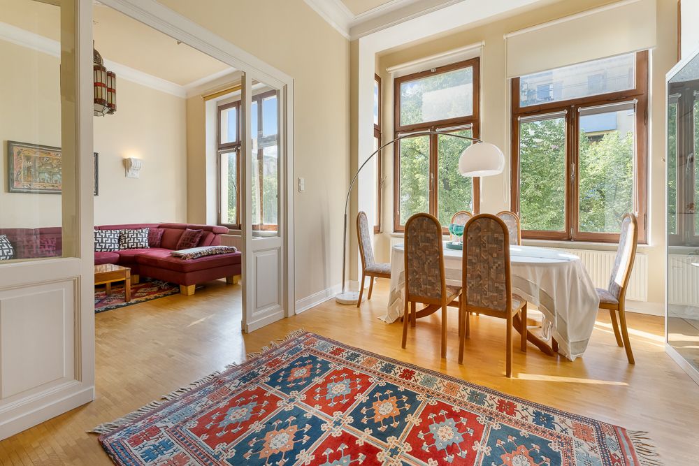 Helles Esszimmer mit großem Teppich, Esstisch und vier Stühlen, daneben Wohnzimmer mit rotem Sofa.