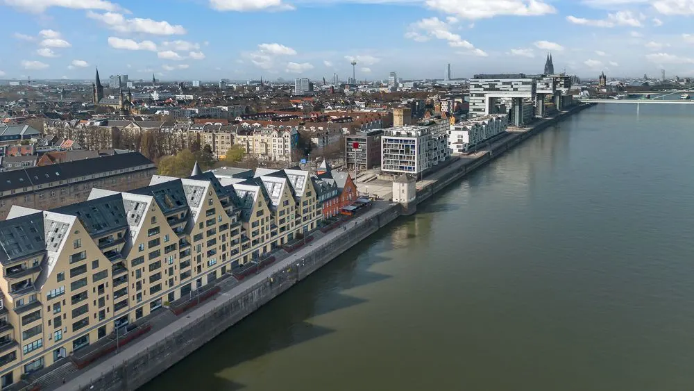 Mehrstöckige Wohnhäuser mit spitzen Dächern am Flussufer, daneben eine lange Uferpromenade.