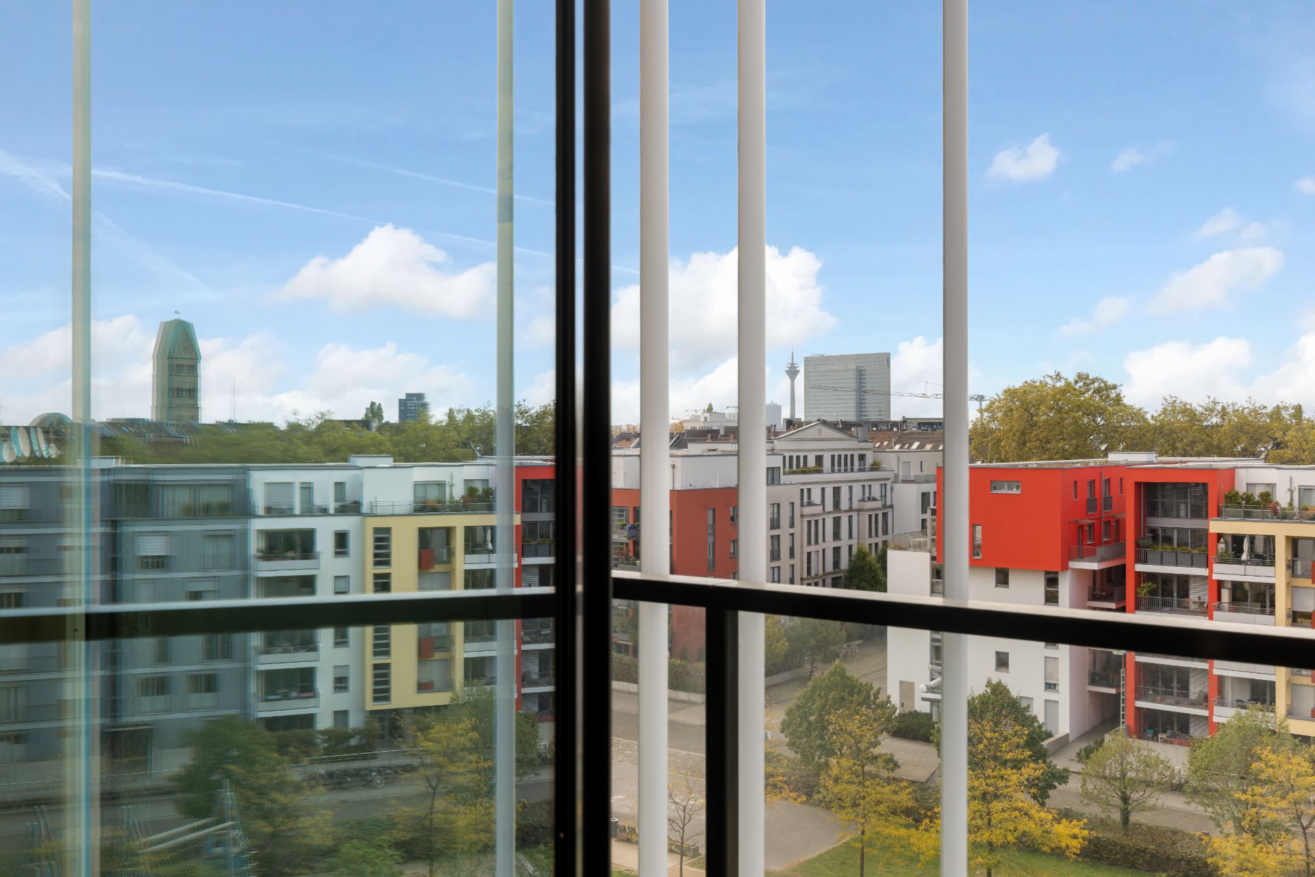Blick durch Glasfenster auf moderne Wohngebäude und Bäume bei klarem Himmel.